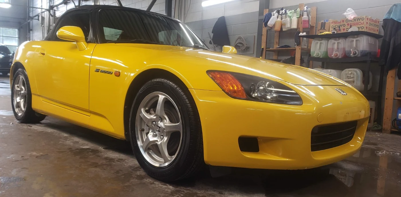 Honda S2000 jaune propre, vue basse mettant en valeur les reflets